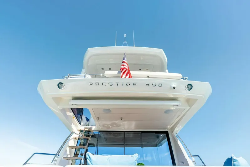 Anna Louise Yacht Photos Pics 2022 Prestige 590 Flybridge yacht with American flag, viewed from the rear under clear blue sky.