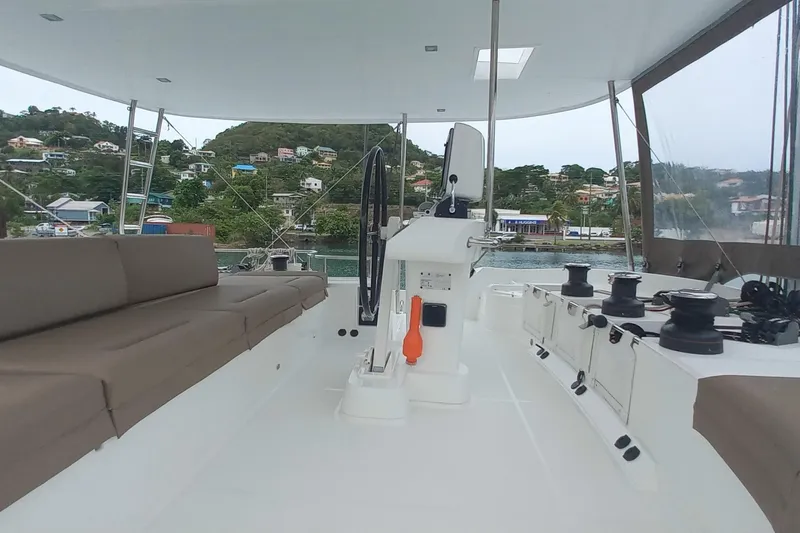 Amea Yacht Photos Pics 2014 Lagoon 52 F catamaran deck with seating and steering wheel, docked near lush hillside.