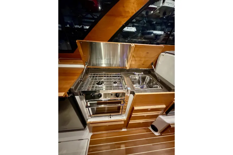  Yacht Photos Pics 2023 Cutwater C-30 Sedan interior kitchen with stove and sink, featuring wood cabinetry.