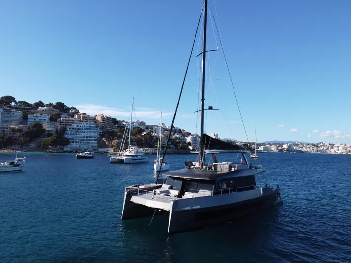 2026 Moon 60 Sail New Yacht Photos Pics Modern 2026 Moon 60 Sail yacht in scenic coastal harbor with buildings and clear blue sky.