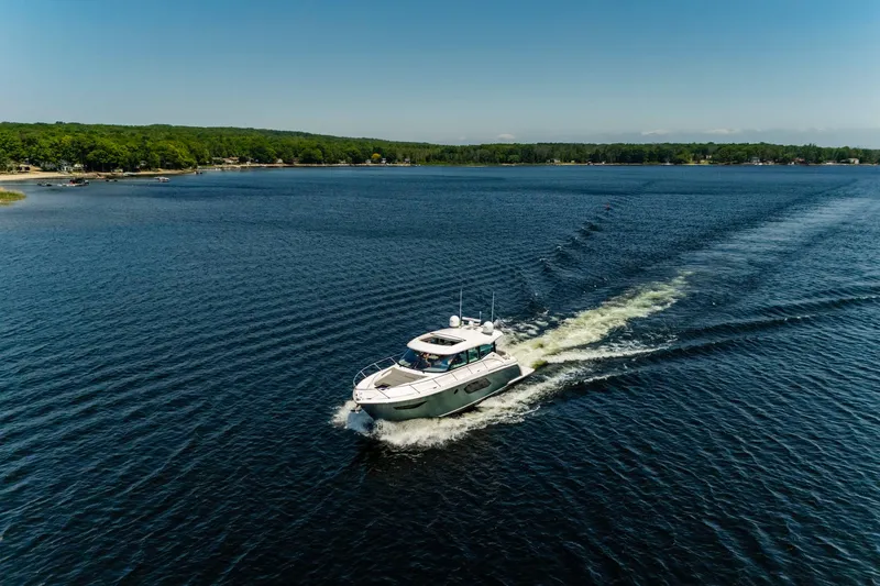  Yacht Photos Pics 2019 Tiara Yachts C49 Coupe cruising on a serene lake under a clear blue sky.