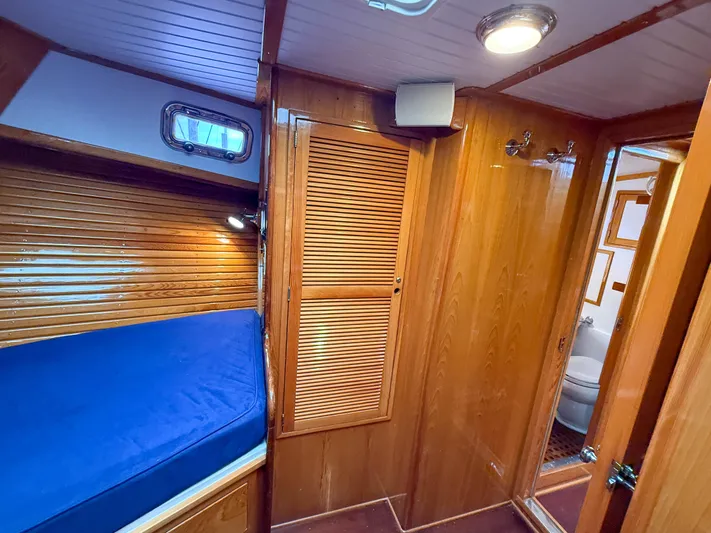 Argonaut Yacht Photos Pics Wood-paneled cabin interior of 1984 Wilbur 38 boat with blue bedding and bathroom view.