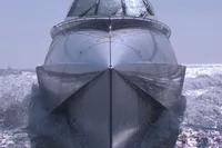Custom VSV yacht from 2007 cutting through waves, front view.