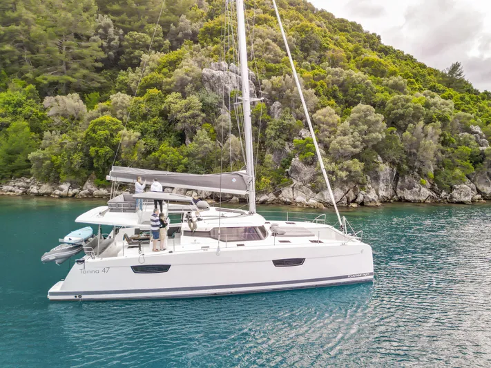  Yacht Photos Pics 2023 Fountaine Pajot Tanna 47 catamaran sailing near lush green coastline.