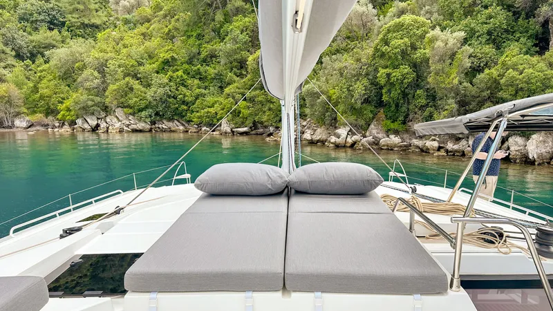  Yacht Photos Pics 2023 Fountaine Pajot Tanna 47 catamaran with sunbeds, anchored in a lush, scenic bay.