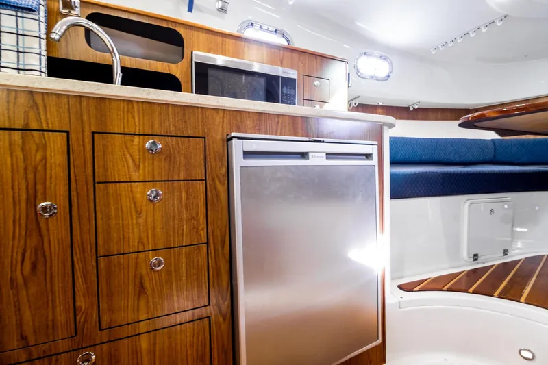 Let&rsquo;s Go II Yacht Photos Pics 2013 Pursuit OS 345 Offshore boat interior with wood cabinetry, fridge, and seating area.