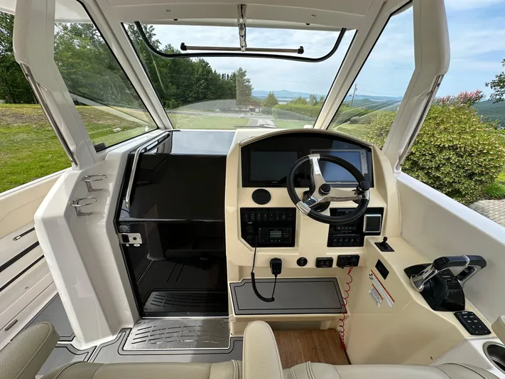  Yacht Photos Pics 2019 Regal 33 SAV boat cockpit with steering wheel and control panel, surrounded by scenic greenery.