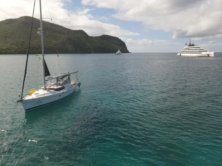 Momentum Yacht Photos Pics Sailboat "Hunter 45 Center Cockpit" anchored near lush island, with luxury yacht in background.