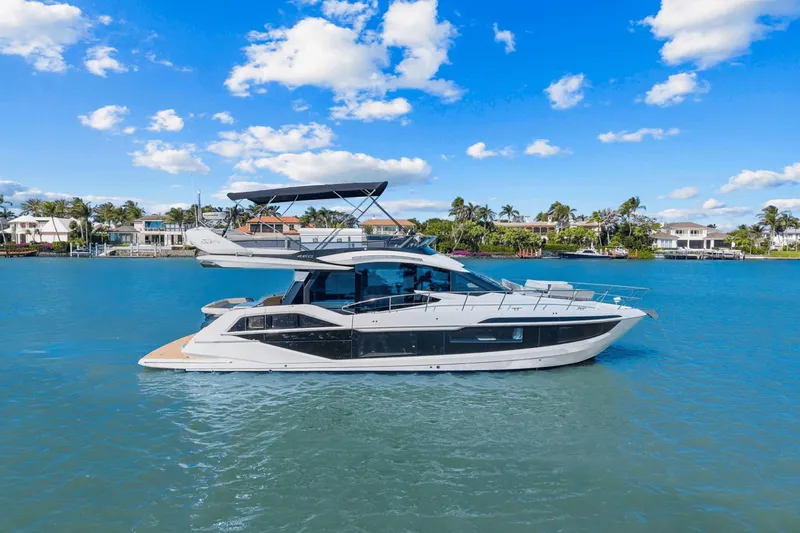  Yacht Photos Pics 2025 Galeon 480 Fly yacht cruising on a sunny day, with waterfront homes in the background.