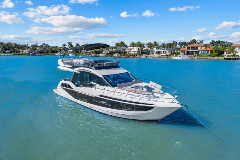  Yacht Photos Pics 2025 Galeon 480 Fly yacht on serene blue water, luxury waterfront homes in background.