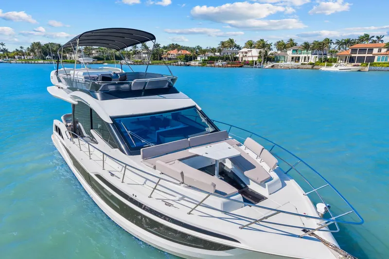  Yacht Photos Pics 2025 Galeon 480 Fly yacht cruising on clear blue water, luxury waterfront homes in background.