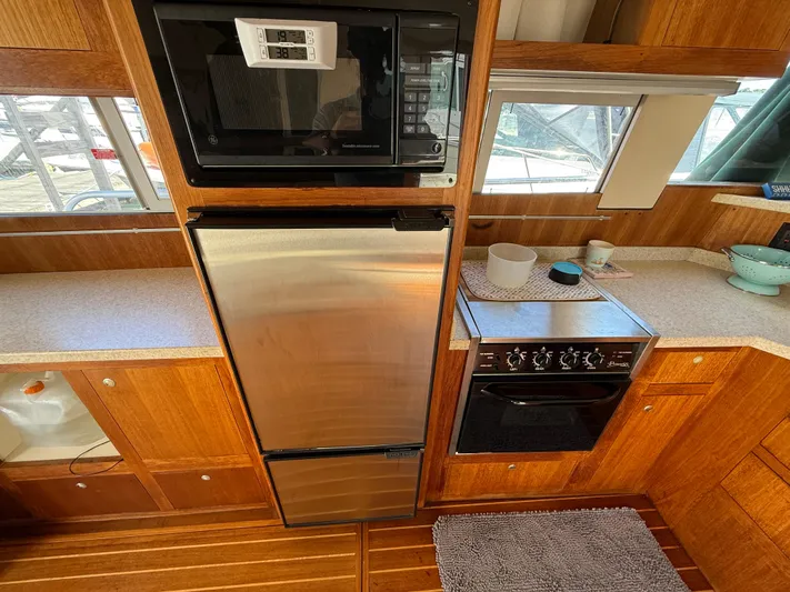 Real Therapy Yacht Photos Pics 2001 Mainship 390 Trawler kitchen with microwave, fridge, and oven in wooden cabinetry.