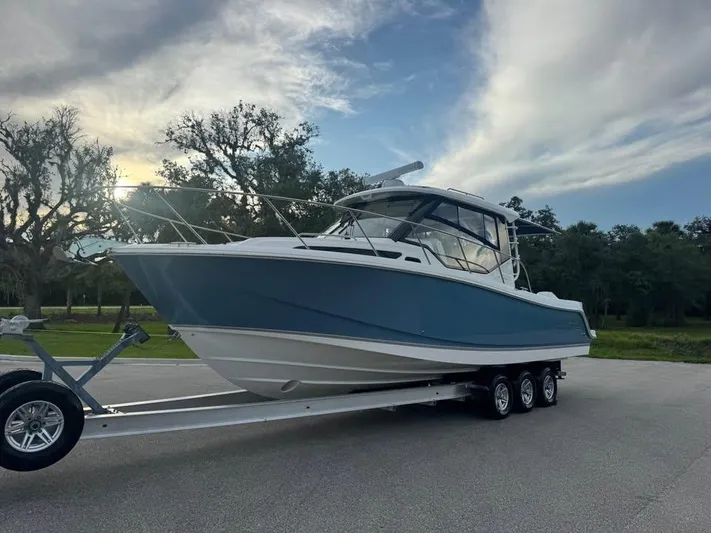  Yacht Photos Pics 2023 Boston Whaler 325 Conquest boat on trailer, parked outdoors under cloudy sky.