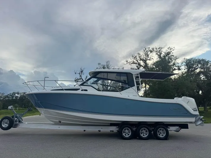  Yacht Photos Pics 2023 Boston Whaler 325 Conquest boat on trailer, parked outdoors under cloudy sky.