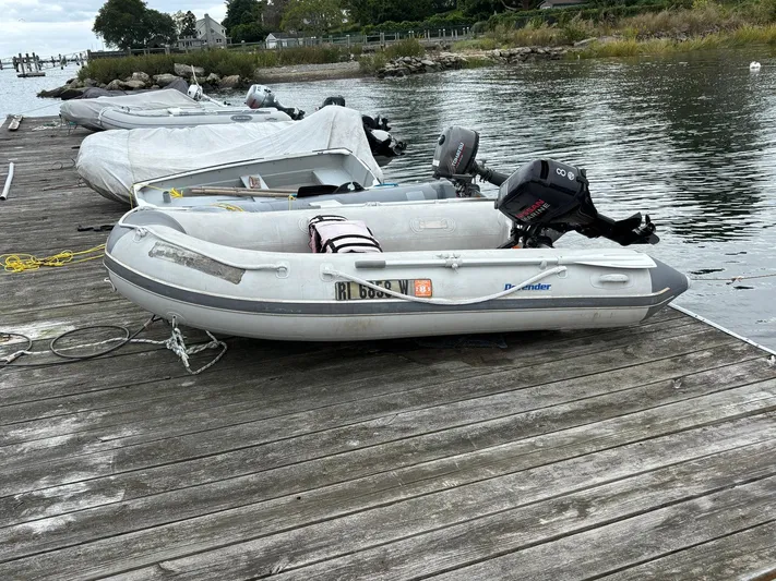 Unbridled Yacht Photos Pics Inflatable boat docked on wooden pier, featuring an outboard motor, near calm waters.