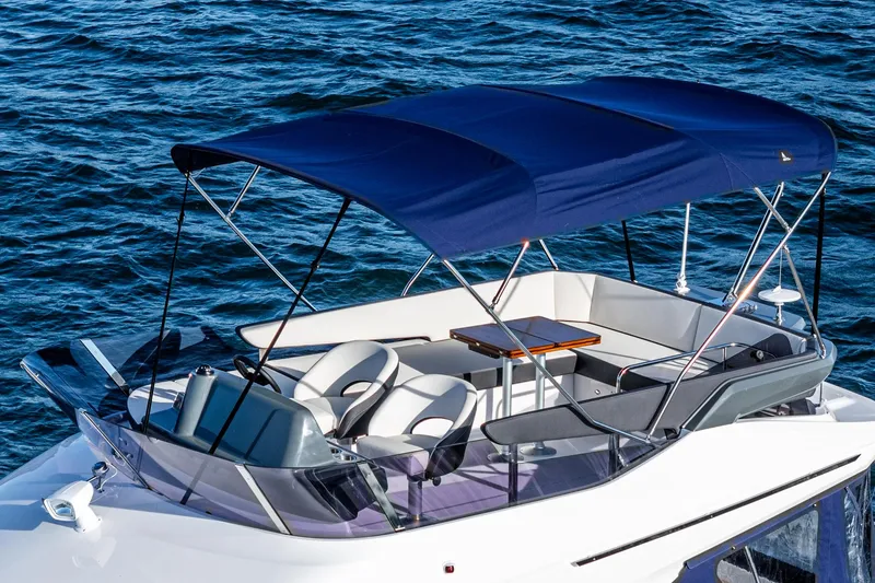  Yacht Photos Pics 2024 Bavaria R40 boat with canopy, featuring sleek seating and table, on calm blue water.