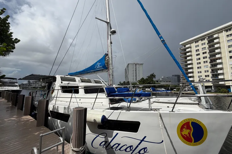 Calacoto Yacht Photos Pics 2023 Royal Cape Catamarans Majestic 530 docked near modern buildings under cloudy sky.