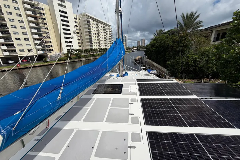 Calacoto Yacht Photos Pics 2023 Royal Cape Catamarans Majestic 530 with solar panels and blue sail, docked near buildings.