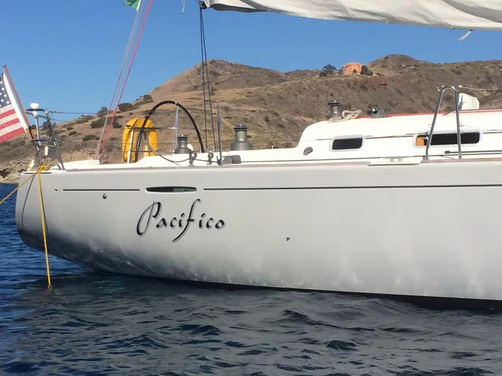 Pacifico Yacht Photos Pics 2005 Beneteau First 44.7 sailboat named "Pacifico" on calm waters near rocky coastline.