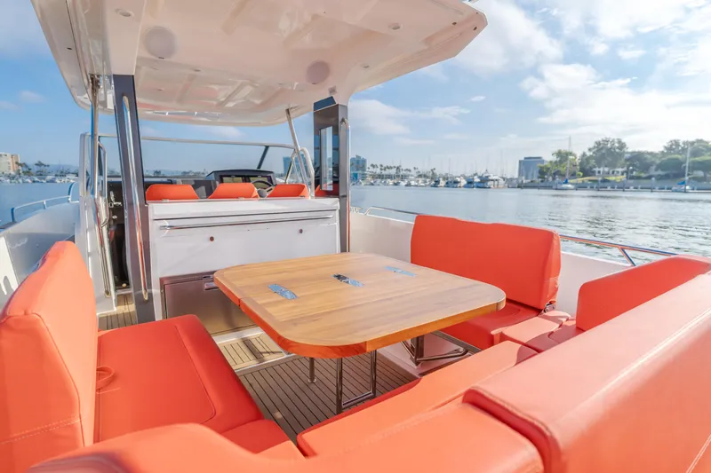 Intrepid Yacht Photos Pics Luxurious 2021 Nimbus T11 boat with orange seating and wooden table, docked by a marina.