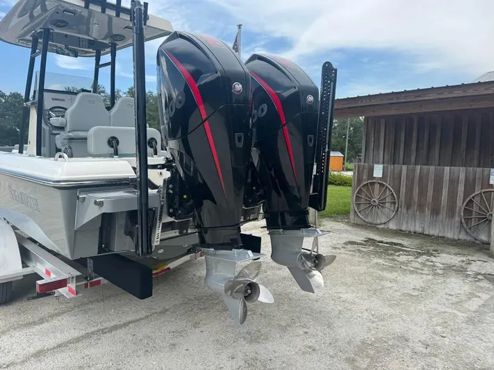  Yacht Photos Pics 2021 ShearWater 270 Carolina Flare boat with dual outboard motors, parked near a wooden shed.