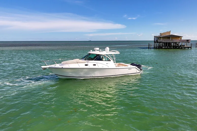  Yacht Photos Pics 2016 Pursuit OS 385 Offshore boat cruising on clear blue water near a stilt house.
