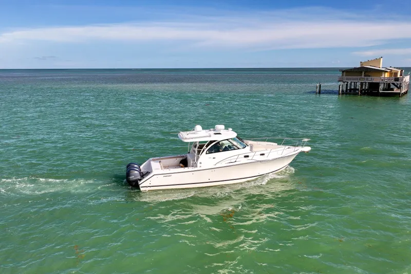  Yacht Photos Pics 2016 Pursuit OS 385 Offshore boat cruising on turquoise waters near a coastal building.