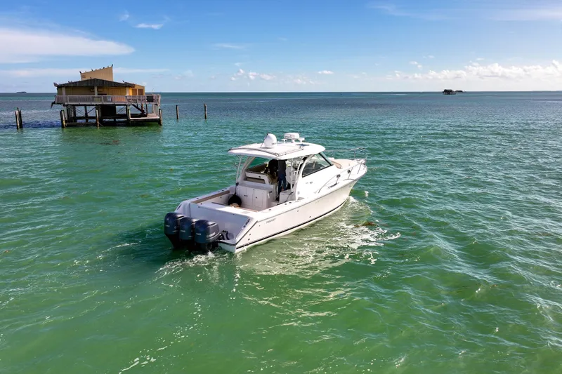 Yacht Photos Pics 2016 Pursuit OS 385 Offshore boat cruising near a stilt house on turquoise waters.