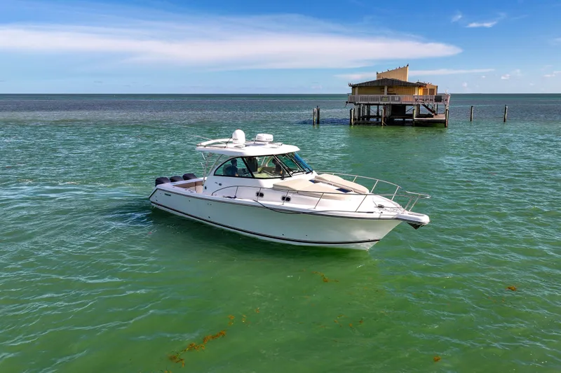  Yacht Photos Pics 2016 Pursuit OS 385 Offshore boat on turquoise water near a stilt house.