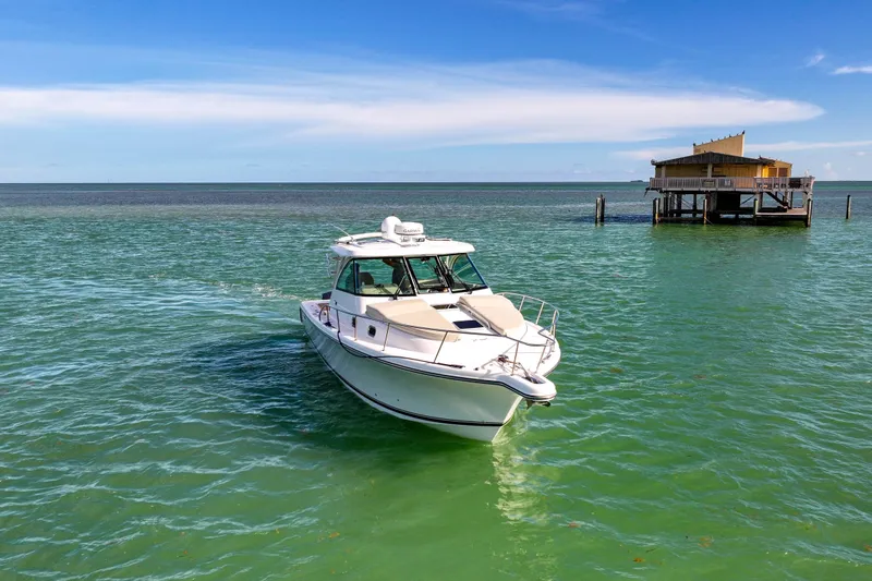  Yacht Photos Pics 2016 Pursuit OS 385 Offshore boat on turquoise water near a stilt house.