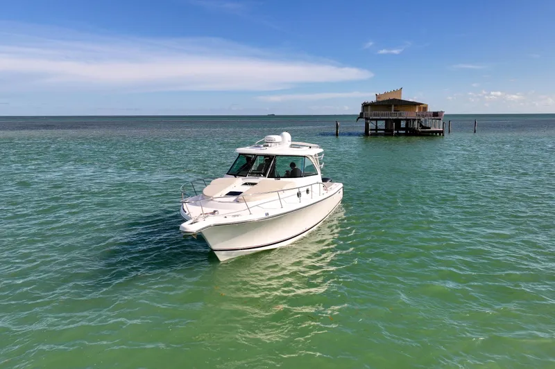  Yacht Photos Pics 2016 Pursuit OS 385 Offshore boat cruising near a stilt house on calm, turquoise waters.