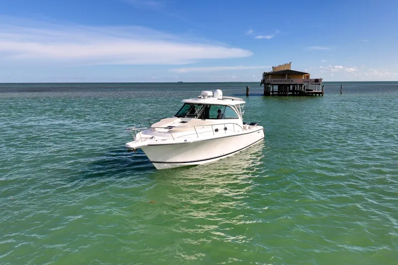  Yacht Photos Pics 2016 Pursuit OS 385 Offshore boat on turquoise water near a stilt house.