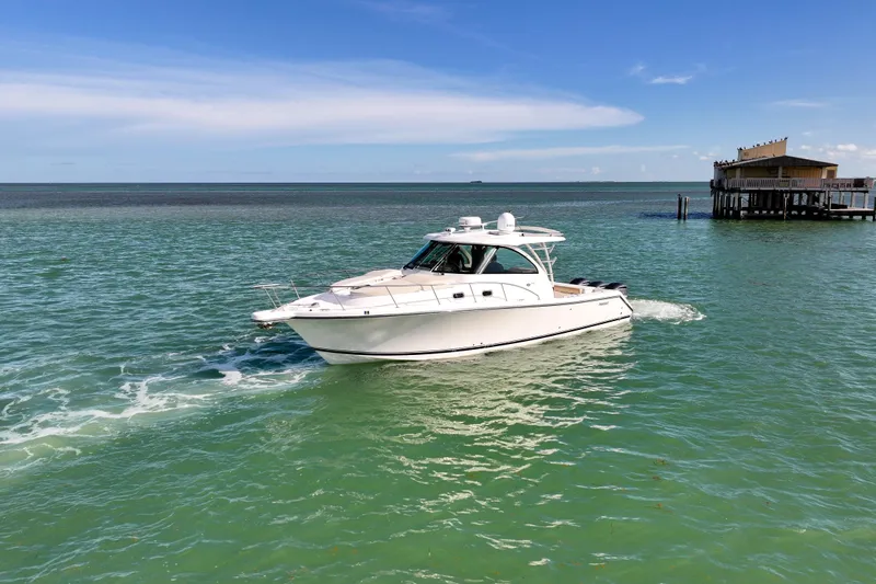  Yacht Photos Pics 2016 Pursuit OS 385 Offshore boat cruising on turquoise waters near a coastal building.