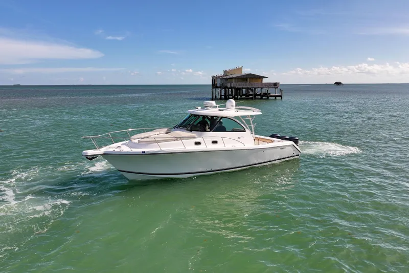  Yacht Photos Pics 2016 Pursuit OS 385 Offshore boat cruising on clear blue waters near a stilt house.