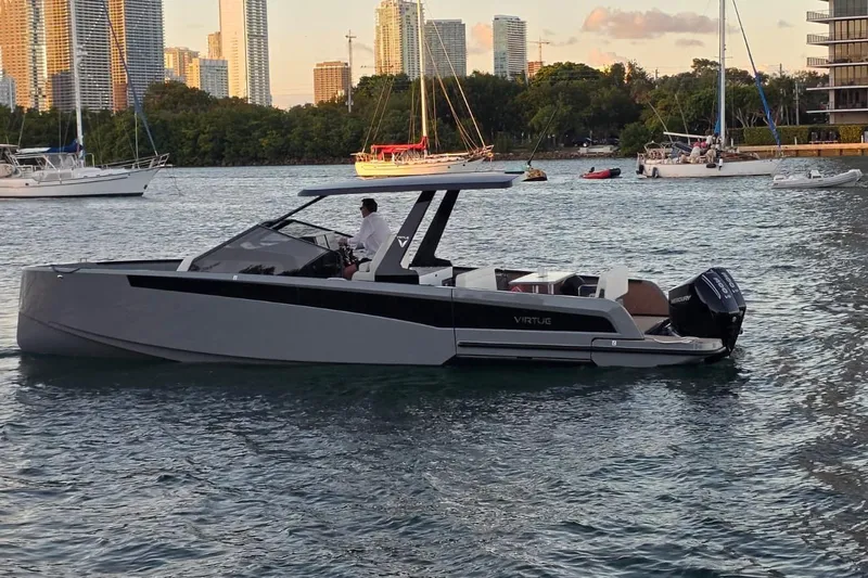 Virtue Yacht Photos Pics 2026 Virtue V10 boat cruising in a scenic harbor with city skyline backdrop.