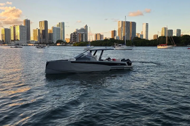 Virtue Yacht Photos Pics Modern Virtue V10 boat cruising near city skyline, 2026 model, with sailboats in the background.
