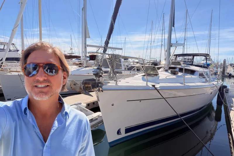 Wailele Yacht Photos Pics Man smiling beside a 2007 Hunter 44 Deck Salon yacht in a marina.