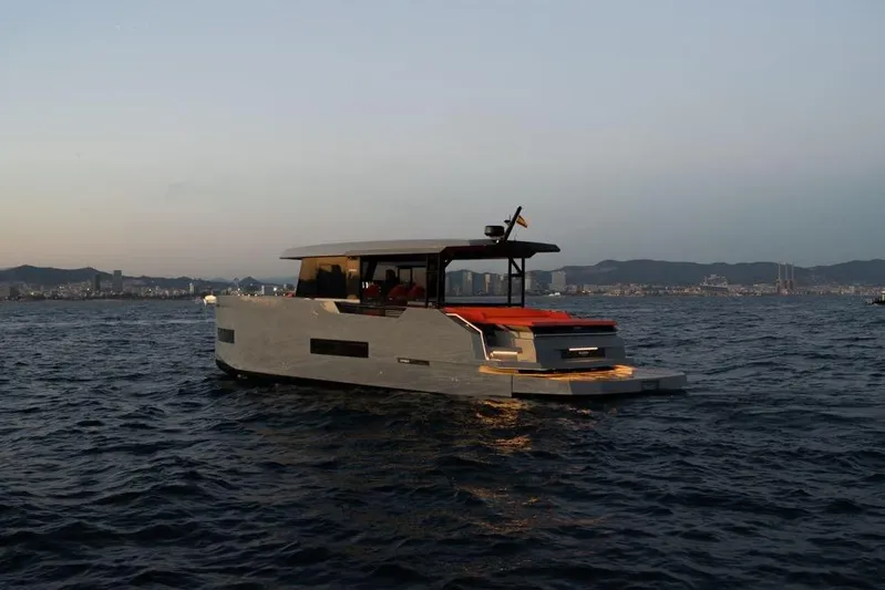  Yacht Photos Pics 2025 De Antonio Yachts D50 cruising at sunset near a coastal city skyline.