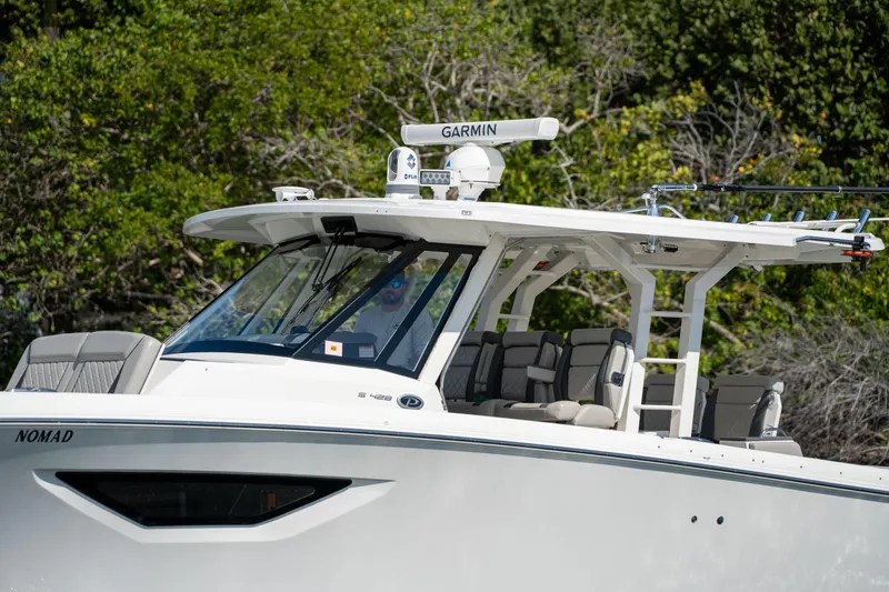 Nomad Yacht Photos Pics 2022 Pursuit S 428 Sport boat with Garmin equipment, docked near lush greenery.