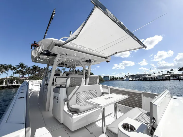 Nomad Yacht Photos Pics 2022 Pursuit S 428 Sport boat with seating area and canopy, docked by palm trees.