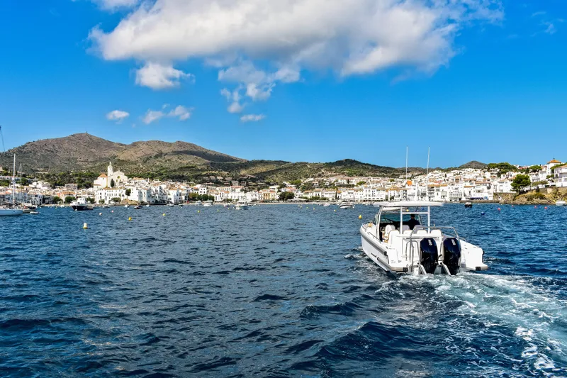 Yacht Photos Pics 2024 Axopar 37 Sun Top cruising in scenic coastal waters with mountains and town in background.
