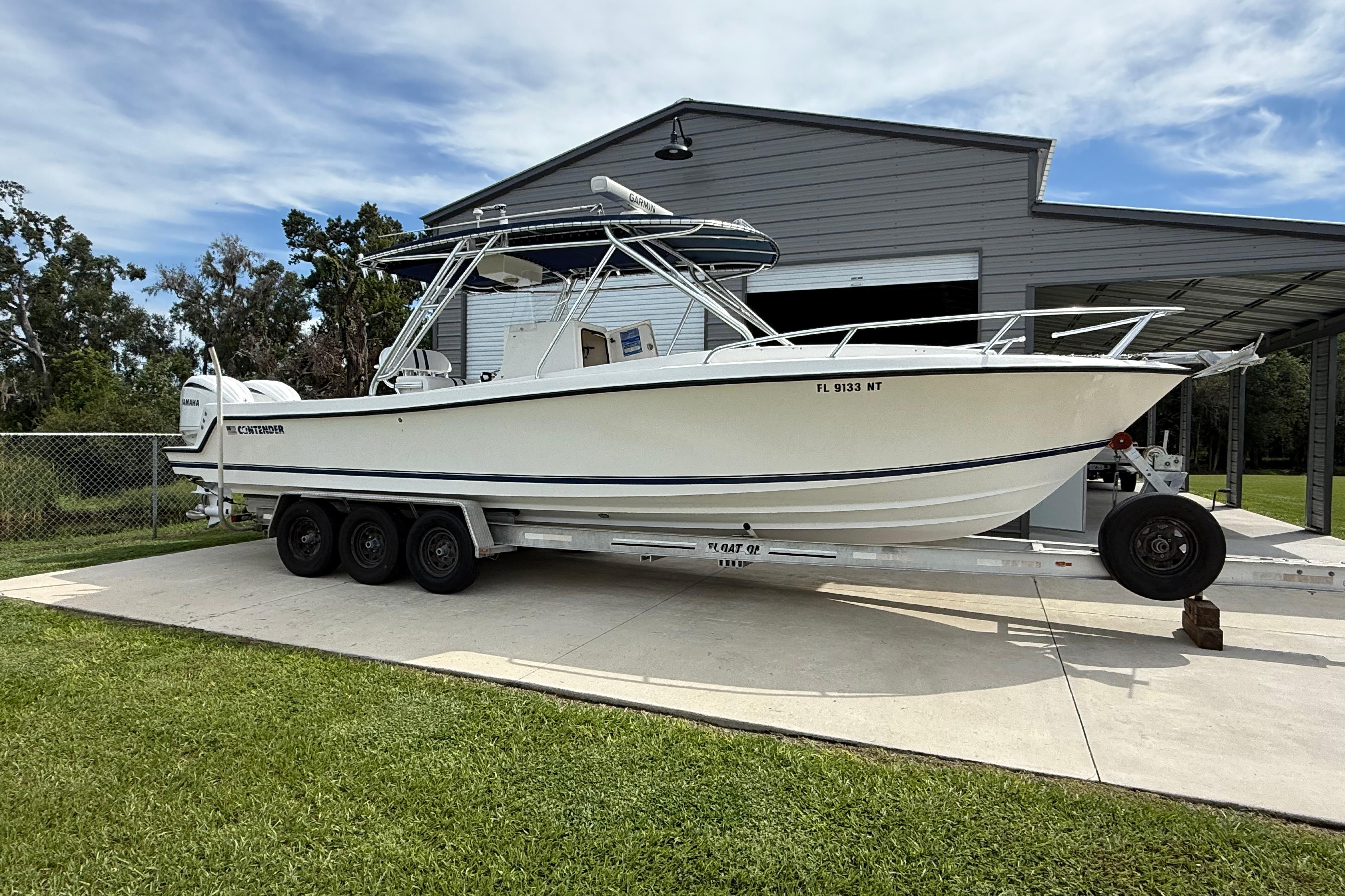 2008 Contender 31 Cuddy boat on trailer, parked near a metal building.