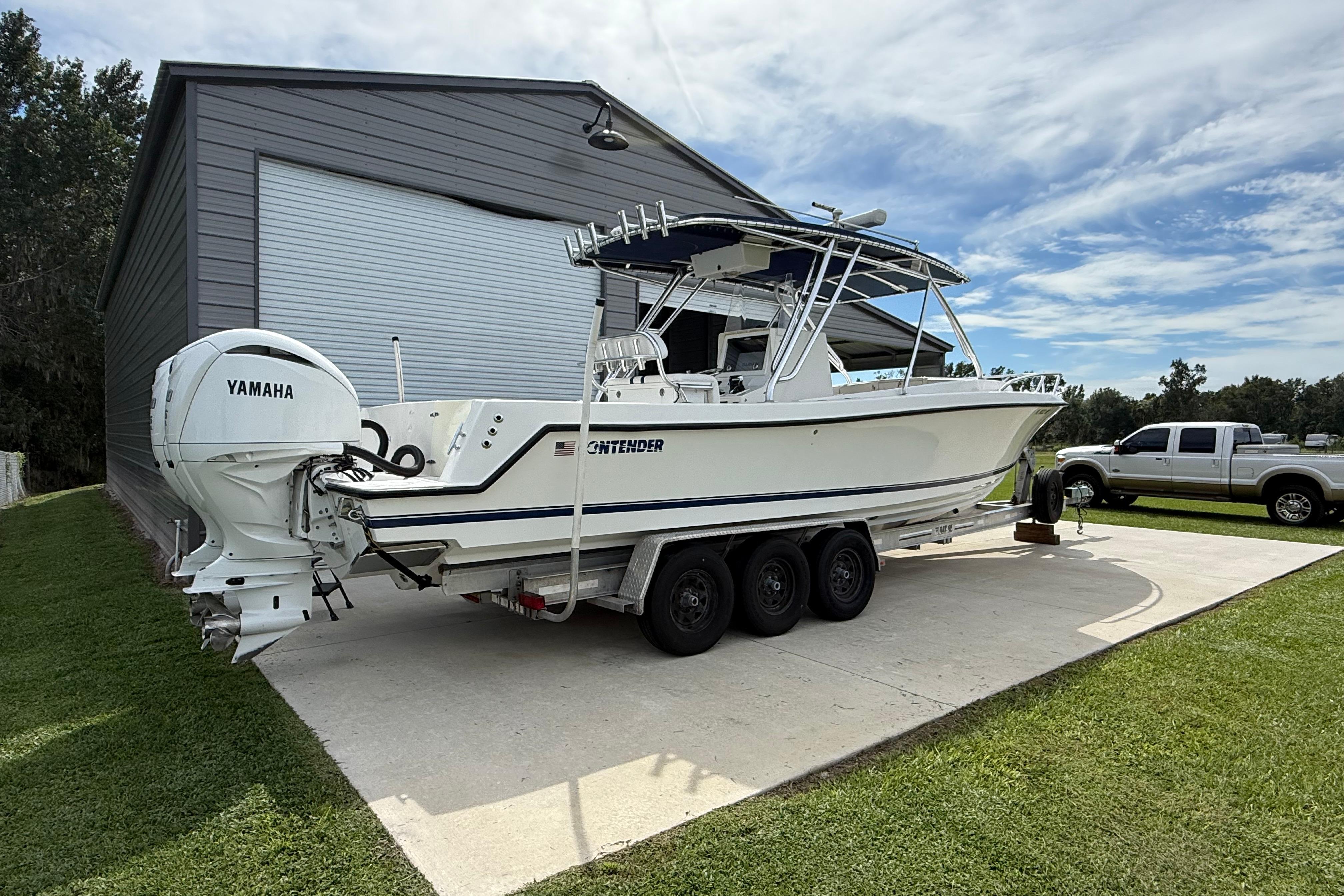 2008 Contender 31 Cuddy boat with Yamaha engines on a trailer near a garage.