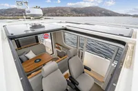 2021 Nimbus C11 boat interior with seating, table, and open roof, overlooking scenic water and mountains.