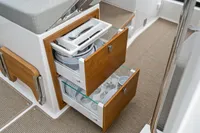 Modern boat kitchen storage with wooden drawers, featuring organized plates and cutlery on Nimbus C11, 2021.