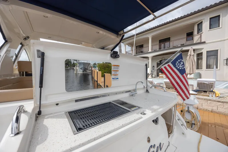  Yacht Photos Pics 2019 Sea Ray Sundancer 350 Coupe with outdoor grill and American flag, docked by a waterfront home.