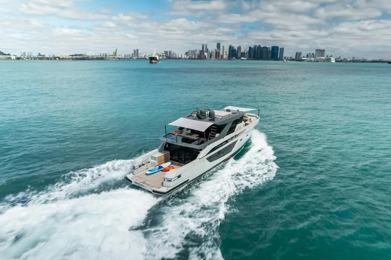  Yacht Photos Pics 2022 Bluegame BGX70 yacht cruising on open water with city skyline backdrop.