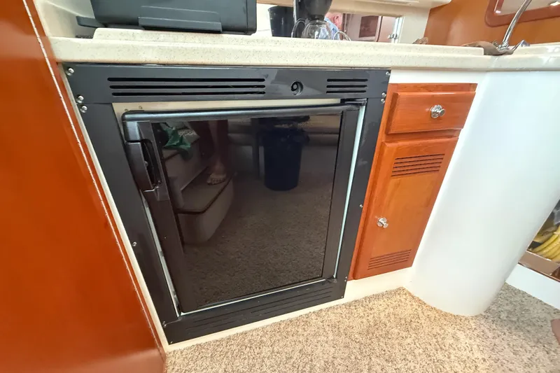 Panacea Yacht Photos Pics 1998 Cabo 31 Express boat interior with compact refrigerator and wooden cabinetry.