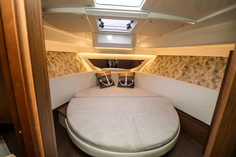  Yacht Photos Pics Cozy cabin interior of 2021 Jeanneau NC 1095 with round bed and decorative pillows.