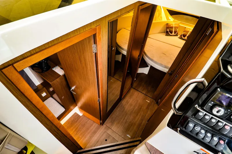  Yacht Photos Pics Interior view of 2021 Jeanneau NC 1095 boat cabin with wooden doors and cozy sleeping area.